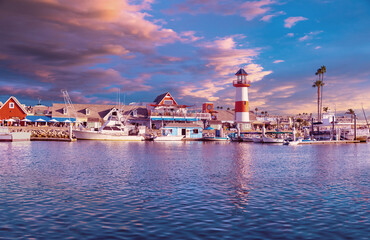 Colorful panorama of Oceanside Harbor at sunset with sky, waterfront and lighthouse reflected in the harbor.