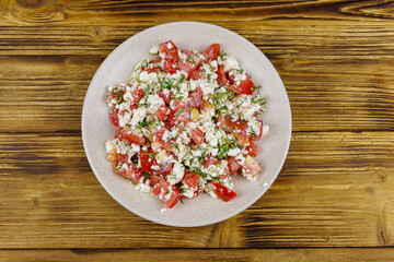 Tasty salad of tomato, cottage cheese, dill and olive oil on wooden table. Top view
