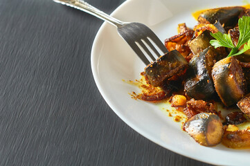 Served dish of fried bananas with onion and curry near metal fork in restaurant on concrete table