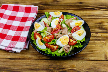 Tasty tuna salad with eggs, lettuce and fresh vegetables on wooden table