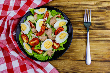 Tasty tuna salad with eggs, lettuce and fresh vegetables on wooden table. Top view