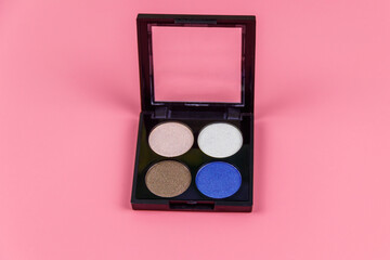 Set of four round eye shadow in a plastic black box on a pastel pink background. Flat lay
