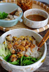tray of Vietnamese vegan food for lunch time, bowl of noodles with deep fried corn spring rolls and sliced cucumber, basil leaf, dipping sauce