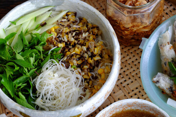 tray of Vietnamese vegan food for lunch time, bowl of noodles with deep fried corn spring rolls and sliced cucumber, basil leaf, dipping sauce