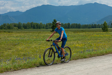 Fototapeta premium A young cyclist rides a mountain bike along a mountain road past against the backdrop of picturesque blue mountains.
