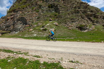 A young cyclist rides along a mountain road past a sheer stone cliff.