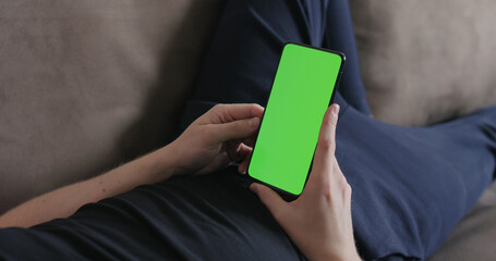 Closeup young man lying on a couch and holding smartphone with green screen