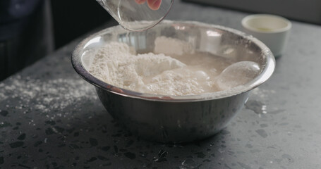 Fototapeta na wymiar wet ingredients into flour in steel bowl on concrete countertop