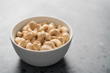 Dry cashew nuts in white bowl on concrete background with copy space