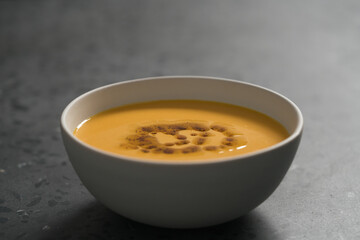 Pumpkin soup decorated with herbs and olive oil in white bowl on concrete background
