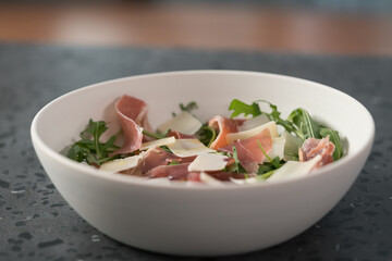 Salad with prosciutto, parmesan and arugula in white bowl on concrete surface