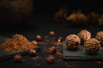 Chocolate candies sprinkled with hazelnut on a black plate and cocoa