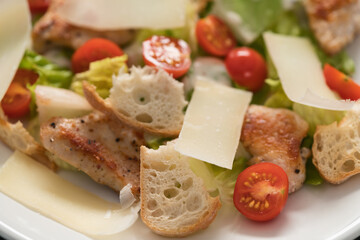 Fresh caesar salad with chicken and cherry tomatoes in white bowl