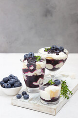 Tiramisu. Homemade dessert in glasses with blueberries, cream and ladyfingers garnish with blueberries and thyme. Light grey stone background.