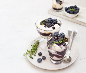 Tiramisu. Homemade dessert in glasses with blueberries, cream and ladyfingers garnish with blueberries and thyme. Light grey stone background.