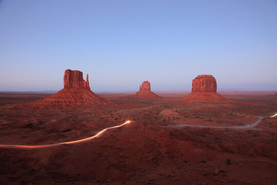 View of The mittens in Monument Valley tribal park with drive road light trails at sunset in Arizona, USA