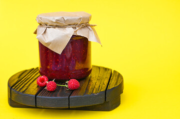 Homemade raspberry jam in a jar on the wooden stand.