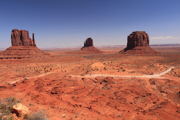 View of The mittens in Monument Valley tribal park with cars driving on valley dirt road in Arizona, USA