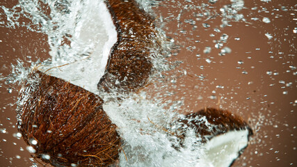 Cracked coconut in freeze motion, isolated on light brown background