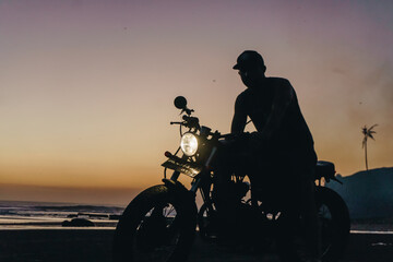Obraz na płótnie Canvas Male model on a custom bike during sunset in the beach