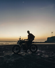 Fototapeta na wymiar Male model on a custom bike during sunset in the beach