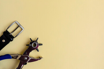 Flat lay of portable leather hole puncher and black belt on the yellow background. Copy space. The...