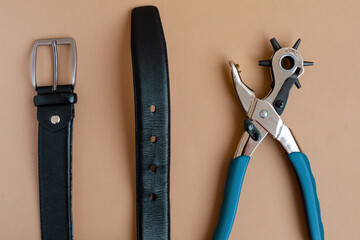 Flat lay of portable leather hole puncher and black belt on the yellow background. Copy space. The...