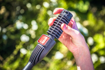 Closeup of a hand holding the handle of high pressure washer. Blurred green background outdoors.