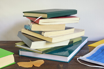 Autumn concept. Stack of books, yellow leaf, face protective mask. Free space for text