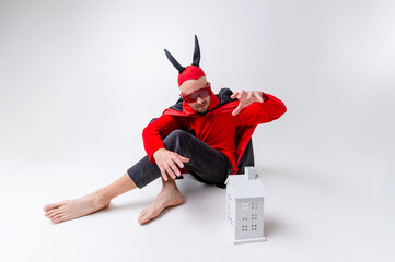 Young man in halloween devil cape and sunglasses with decorative building over white background.