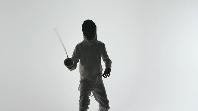 Dark silhouette of fencer training fencing exercise in studio indoors. Athlete is practicing an attack on an opponent. Shot isolated on white background. Slow motion. Close up.