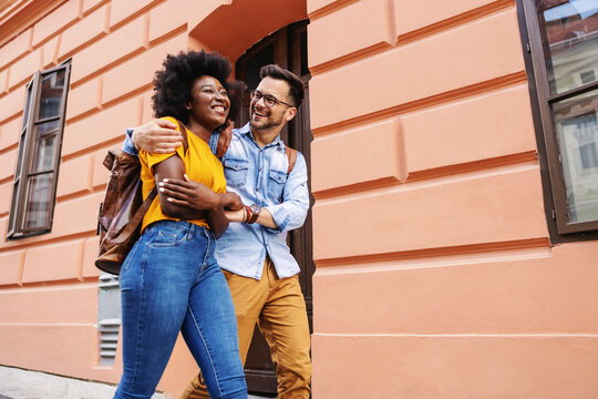Young attractive multicultural couple hugging and walking on the street. - Powered by Adobe