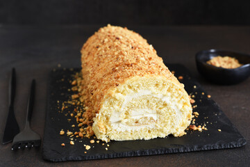 Biscuit roll with cream and nuts on a slate blackboard on a dark background.