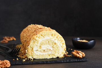 Biscuit roll with cream and nuts on a slate blackboard on a dark background.