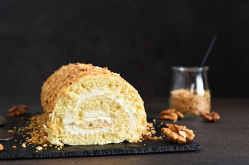 Biscuit roll with cream and nuts on a slate blackboard on a dark background.