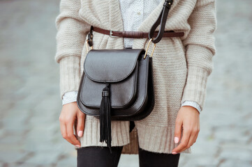 Fashionable young woman in black jeans, beige cardigan and black handbag . Street style