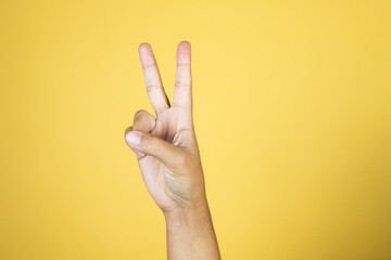 Naklejka premium Hand over isolated yellow background showing with fingers number two or peace signal