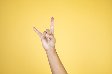 Hand over isolated yellow background doing rock symbol