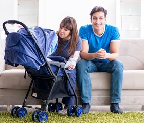 Young parents with their newborn baby in baby pram sitting on th
