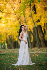 Obraz na płótnie Canvas Beautiful brunette young female in white dress in autumn park