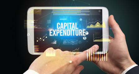 Close-up of hands holding tablet with CAPITAL EXPENDITURE inscription, modern business concept