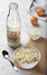 Crumbly cottage cheese on sacking. Homemade cottage cheese on a light background. Still life with cottage cheese, milk and sour cream on a light background.