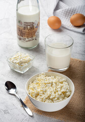 Crumbly cottage cheese on sacking. Homemade cottage cheese on a light background. Still life with cottage cheese, a glass of milk, chicken eggs and sour cream on a light background.