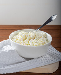 Homemade crumbly cottage cheese on a wooden background. Cottage cheese with a spoon on a wooden Board.