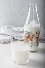 A glass of milk with a bottle of milk in the background, on a light background.