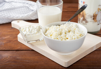 Homemade crumbly cottage cheese on a wooden background. Cottage cheese with a bottle of milk, sour cream and a glass on a wooden background.