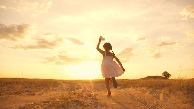 A happy family. A girl in a dress with a paper airplane in her hands runs across a wheat field. The kid plays an aviator and dreams of traveling. A chidhood dream. The kid is holding a toy.