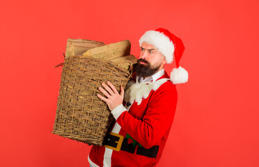 Santa man. Winter holiday. Basket of chopped firewood. Bearded man in Santa claus costume with basket of firewood. Merry Christmas and happy New year. Holiday, rest, gifts, winter.