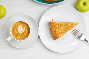 Piece of apple pie with almond petals and cup of coffee cappuccino on white wooden table. Top view.