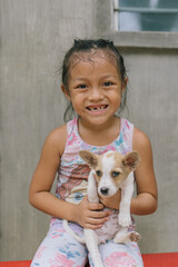 Pretty and Cute Little Girl Playing and Holding her Small Fluffy Dog Puppy at Home in Asia in the Philippines. Toothless Happy Kid with missing Teeth